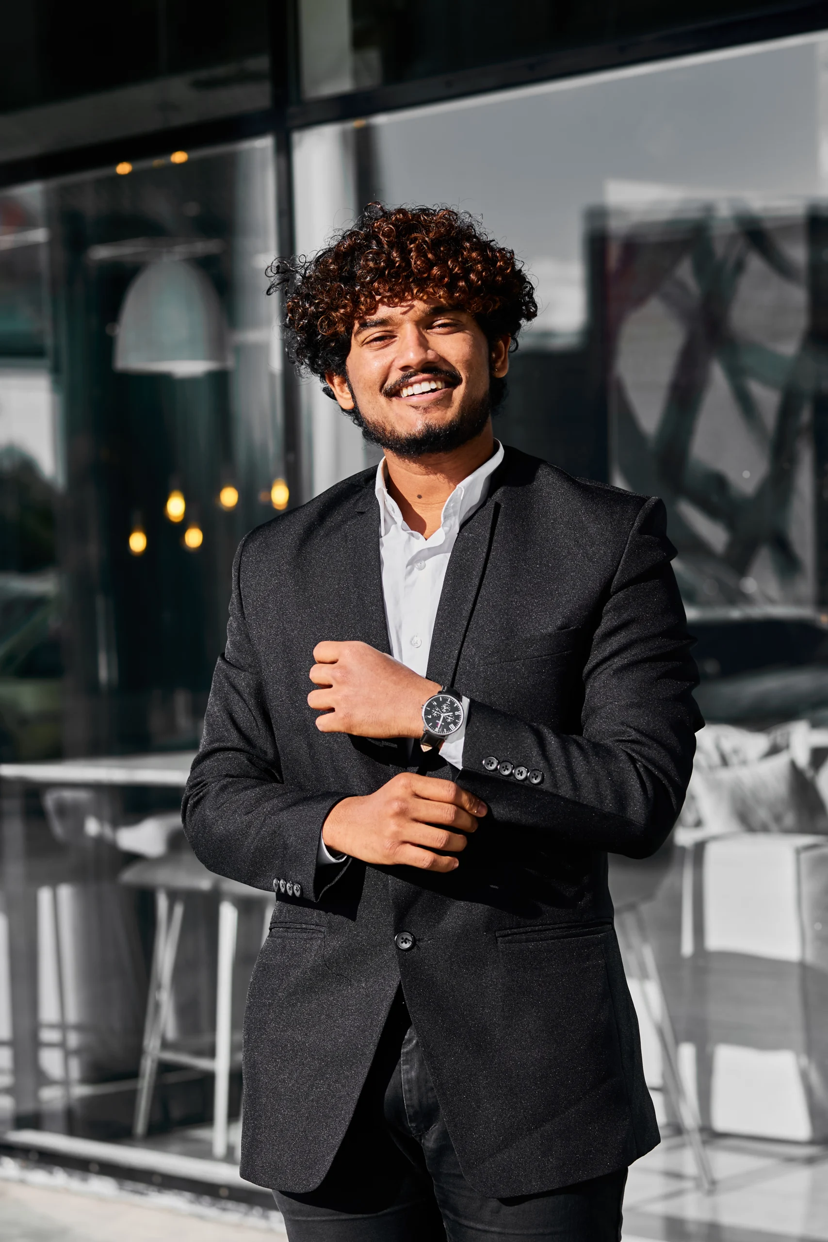 curly haired indian businessman stands outside his office scaled